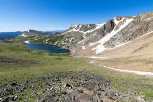 Deep blue alpine lake below a snow-streaked rocky ridge on a green high plateau