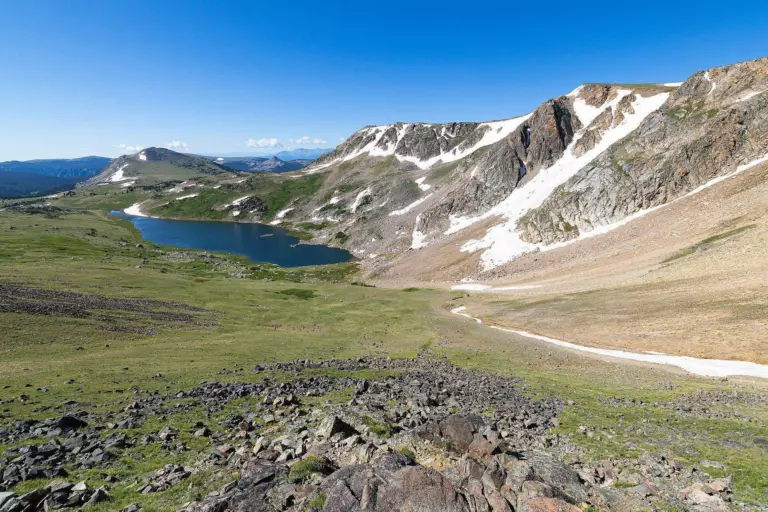 Deep blue alpine lake below a snow-streaked rocky ridge on a green high plateau
