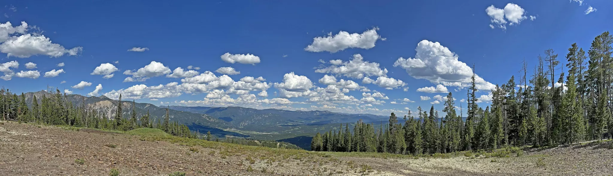 Summer panorama of forested valleys and mountain ridges seen from Mountain Village at Big Sky