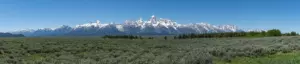 Snow-capped Teton Range rising above a wide sagebrush flat under a clear blue sky