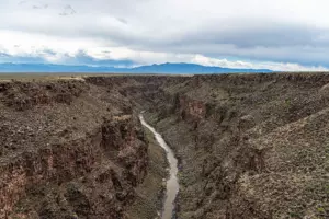 Rio Grande winding through a deep basalt gorge across sagebrush plains, with distant mountains under grey clouds