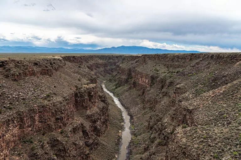 Rio Grande winding through a deep basalt gorge across sagebrush plains, with distant mountains under grey clouds