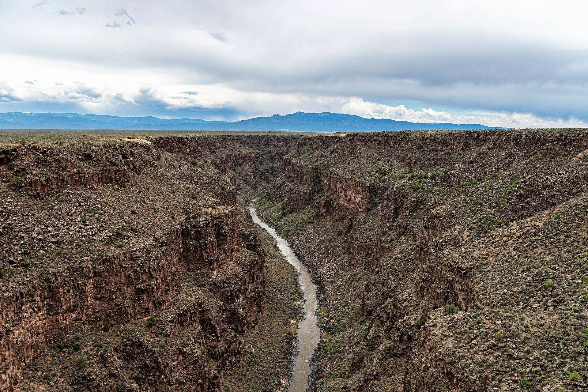 Rio Grande winding through a deep basalt gorge across sagebrush plains, with distant mountains under grey clouds